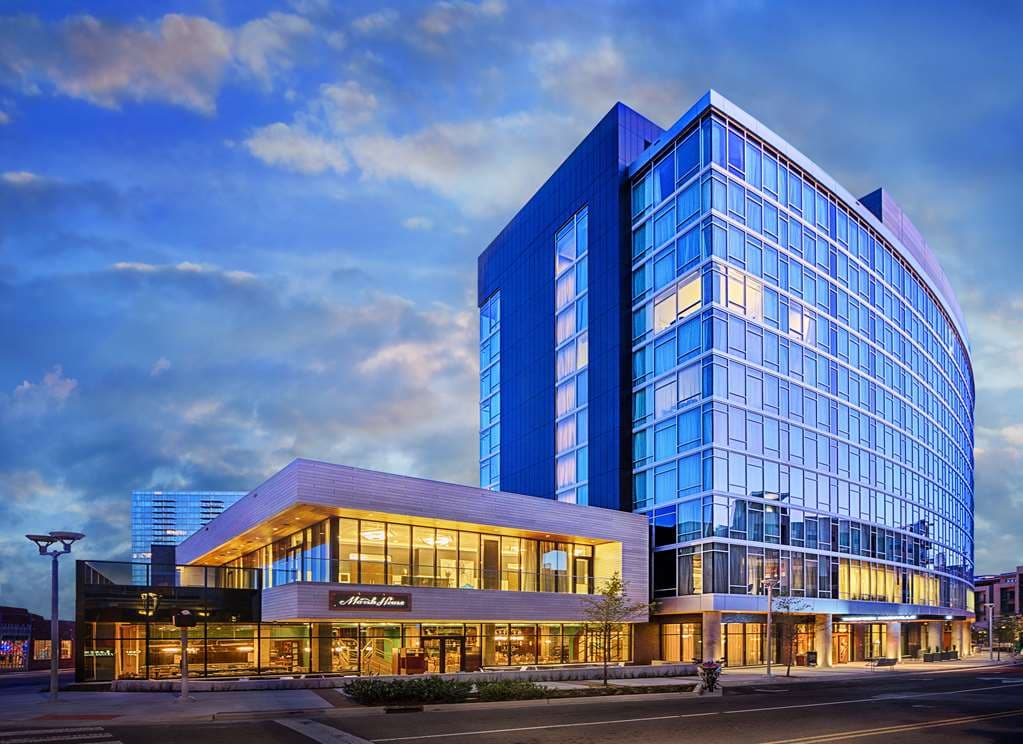 A stylish mid-century modern hotel room at Thompson Nashville featuring floor-to-ceiling windows with a skyline view and a retro wooden bed frame.