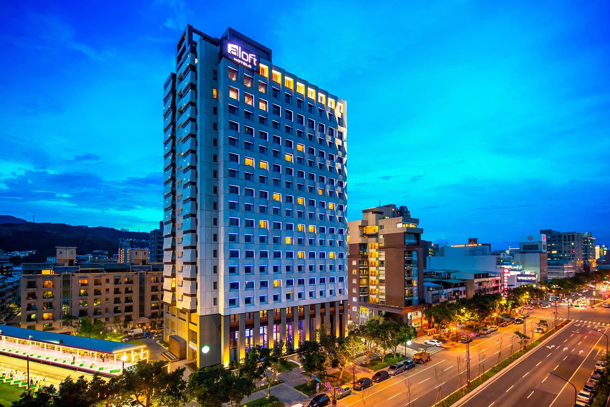 台北北投雅乐轩酒店外观，黄昏时分现代玻璃建筑与霓虹灯光交相辉映，与周围北投住宅区形成对比。