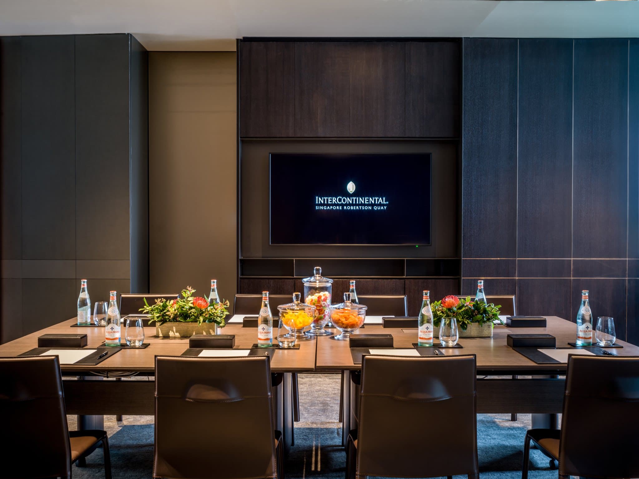 A moody, industrial-chic hotel room at InterContinental Robertson Quay featuring dark wood panels, a plush leather headboard, and floor-to-ceiling windows overlooking the Singapore River.
