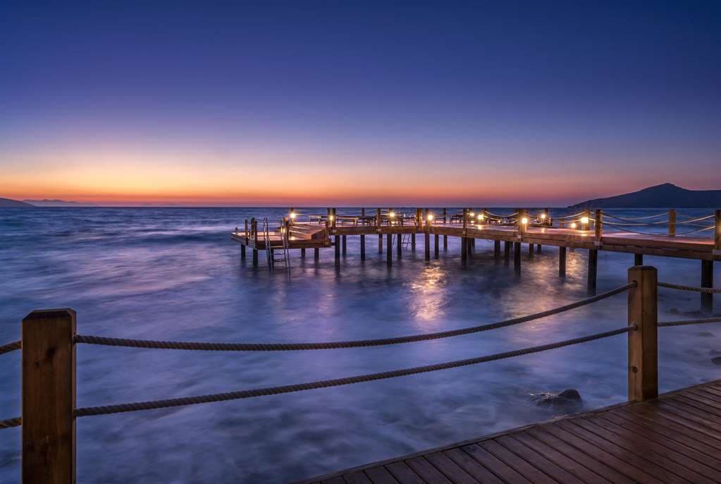 A stunning sunset view over the Allium Bodrum infinity pool, merging seamlessly with the Aegean Sea, framed by wooden decking and chic loungers.