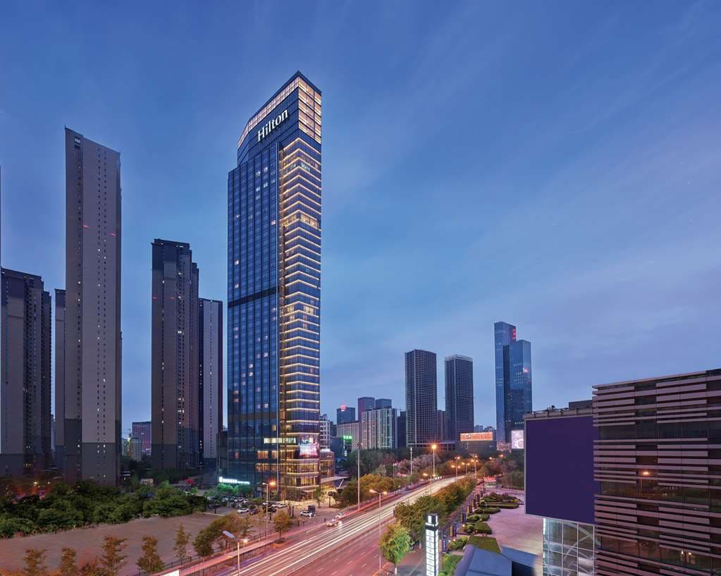 The dramatic, high-ceilinged Song Lobby Lounge at Hilton Shenyang Shimao, featuring floor-to-ceiling windows overlooking a manicured garden.