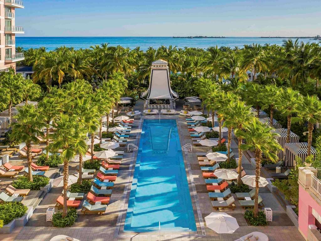 A low-angle shot of the SLS Baha Mar's pink facade featuring white balconies, contrasted against a deep blue Bahamian sky.