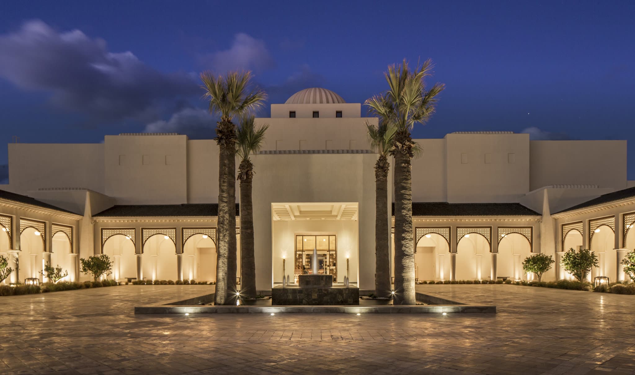 A symmetrical view of the Four Seasons Hotel Tunis Roman-style indoor pool, featuring elegant white arches and turquoise water.