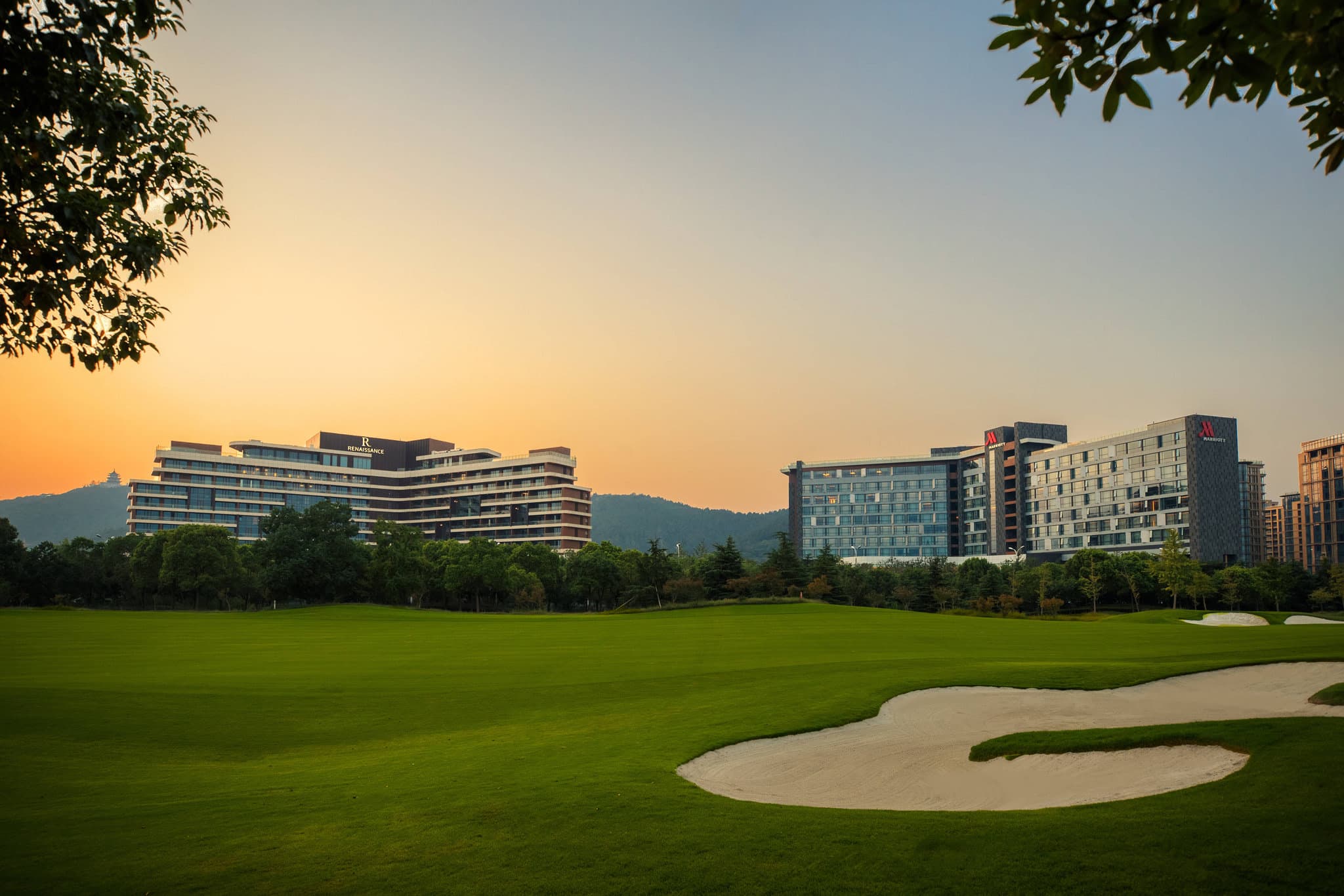 View of the Renaissance Suzhou Taihu Lake Hotel exterior featuring modern geometric architecture against the backdrop of Taihu Lake at sunset.