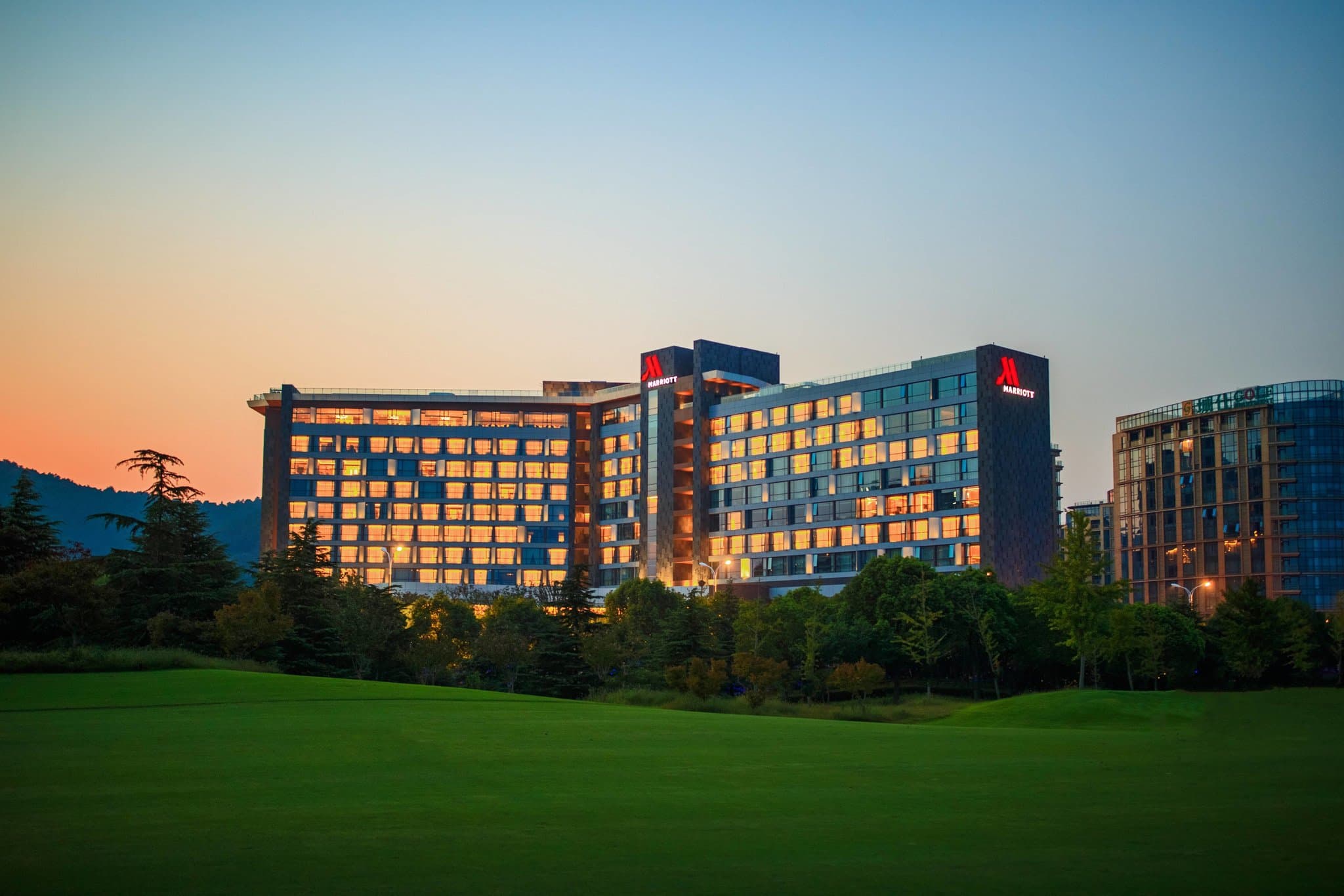 A panoramic view of the Suzhou Marriott Hotel Taihu Lake exterior at dusk, reflecting over the water with distant mountains.