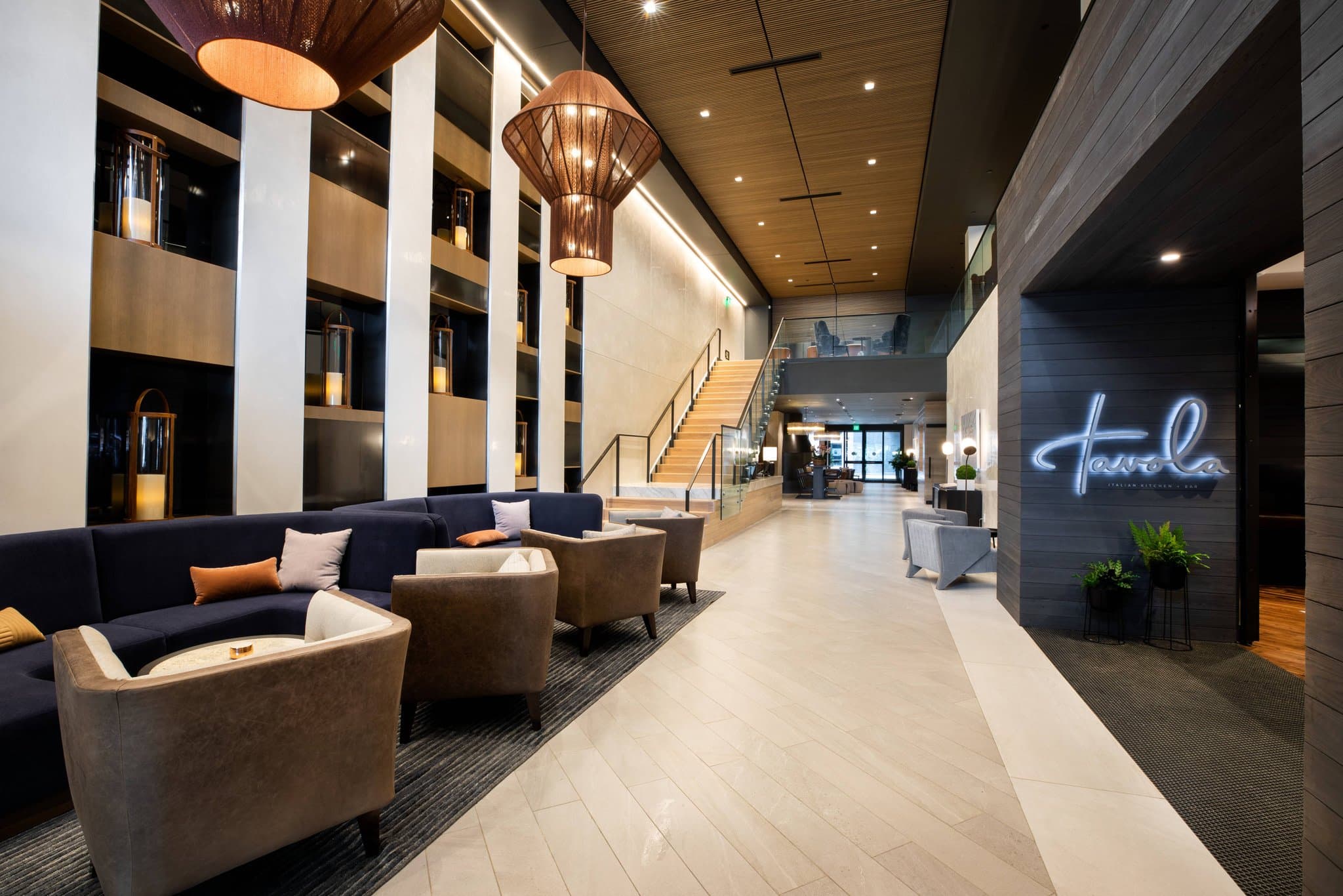 A warm, dimly lit hotel lobby featuring a modern fireplace, Scandinavian furniture, and a floating staircase.