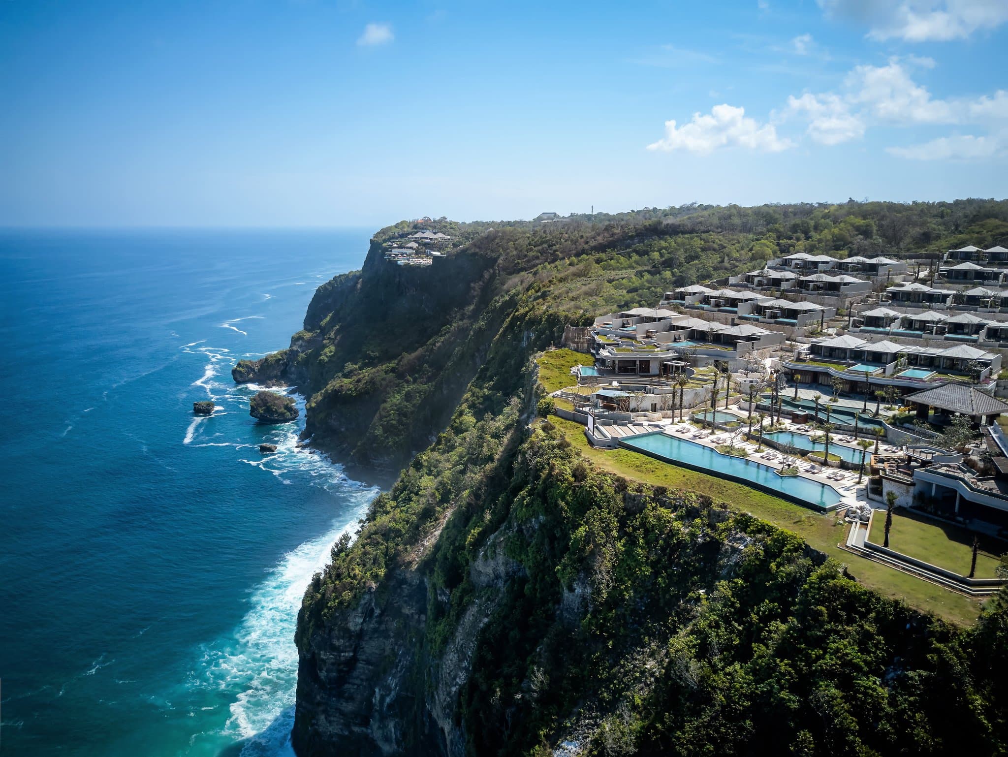 A 100-meter infinity pool at Six Senses Uluwatu stretching along the limestone cliff edge, merging with the Indian Ocean horizon at sunset.