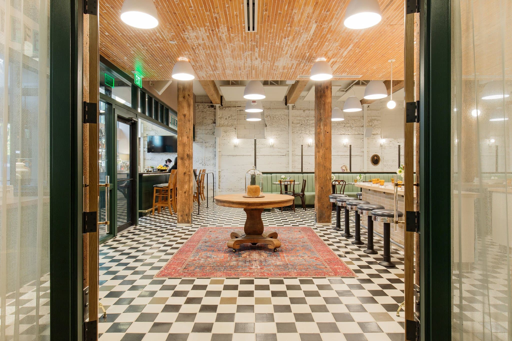 Palihotel Seattle lobby lounge featuring a fireplace, emerald green walls, and a stack of vintage leather suitcases beneath a round mirror.