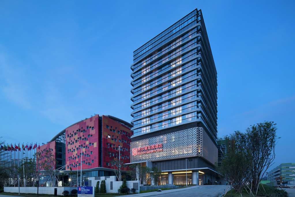 Exterior of Hilton Garden Inn Zhuhai Hengqin featuring the curved 'Soaring Seagull' architecture against a blue sky, located near Sumlodol Camping Town.