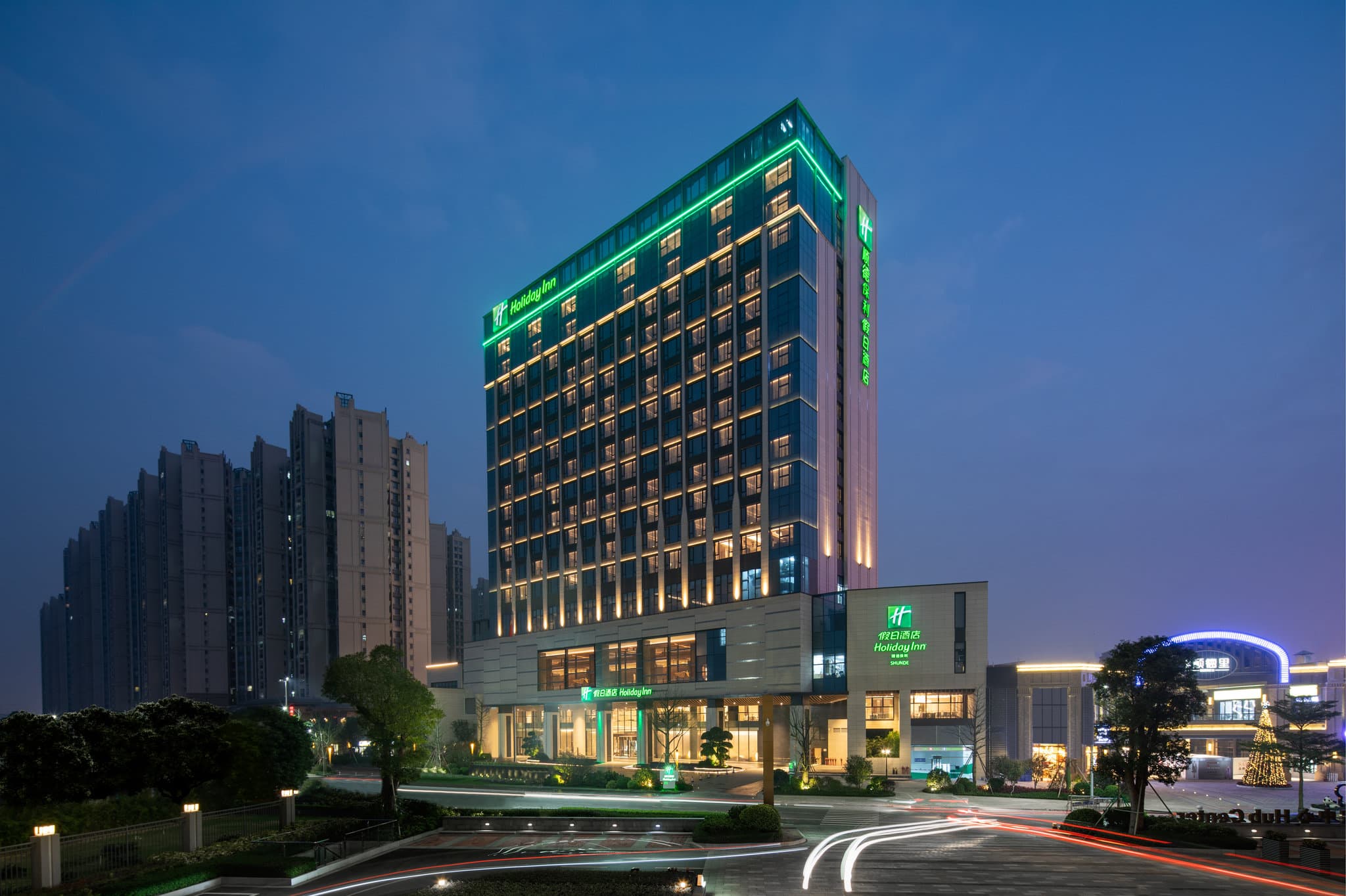 A sleek, modern indoor swimming pool at Holiday Inn Shunde with floor-to-ceiling windows overlooking the city skyline.