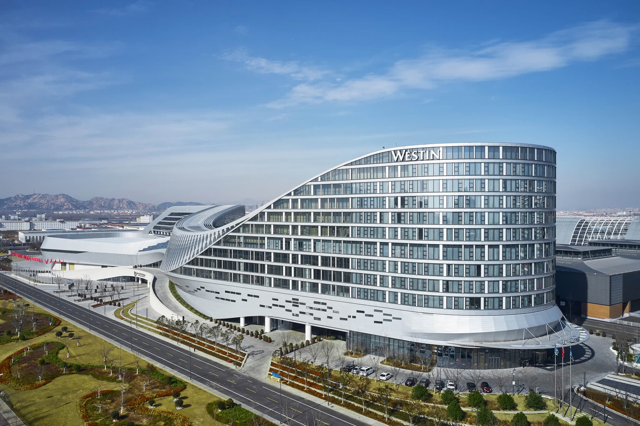 The Westin Qingdao West Coast lobby featuring a grand staircase and biophilic design elements with wood textures.