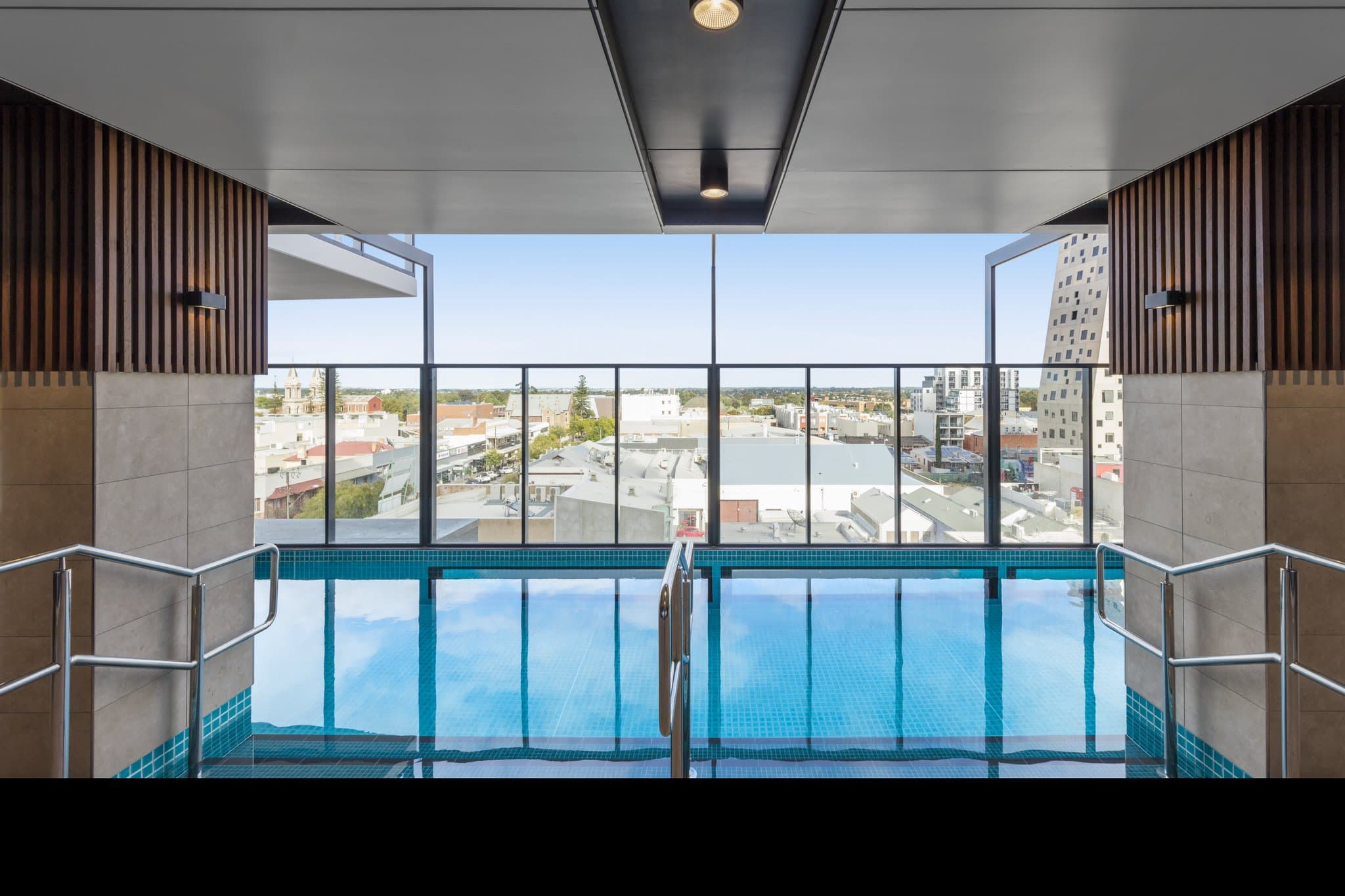 A sleek, modern indoor lap pool on Level 7 of Avani Adelaide Residences, bathed in natural light with city views through floor-to-ceiling windows.