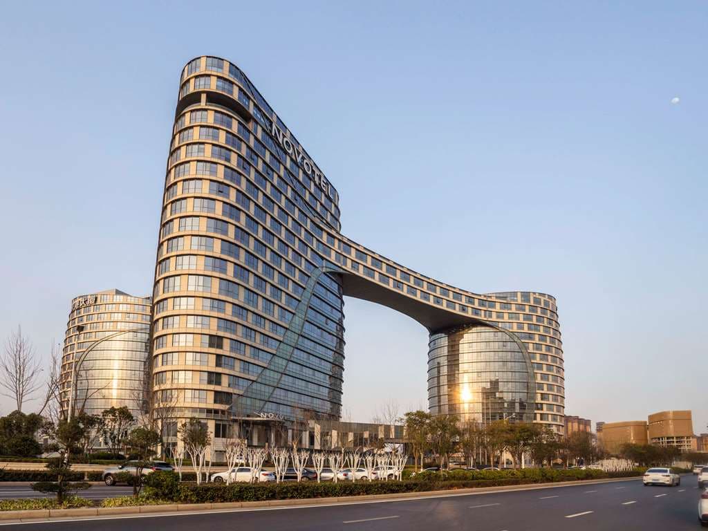 A sleek, blue-tiled indoor swimming pool at Novotel Zhengzhou Airport with floor-to-ceiling windows showing a blurred airport tarmac in the distance.