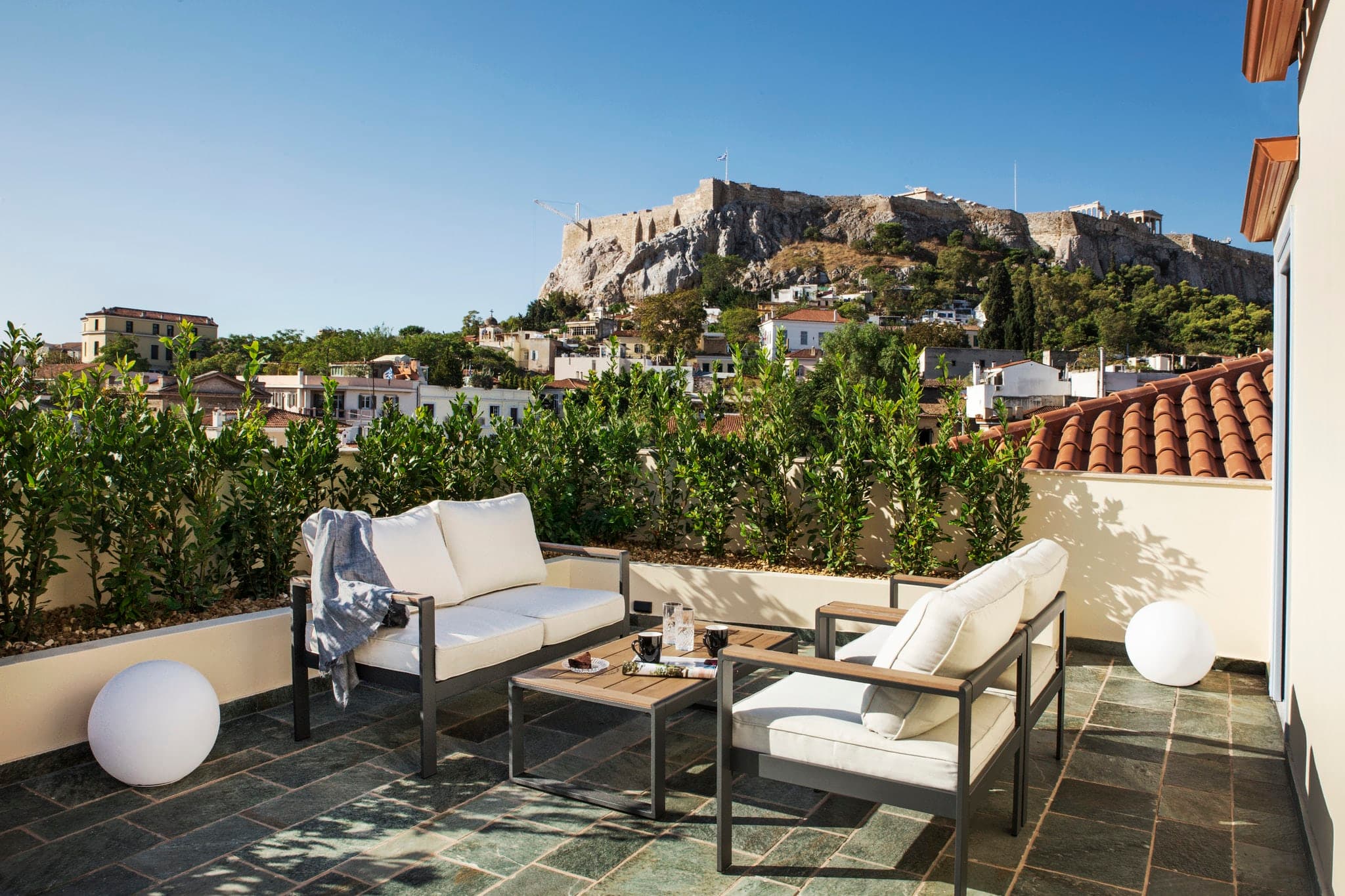 A woman in a white robe relaxing in a private terrace jacuzzi at A77 Suites, with the Parthenon and Acropolis hill perfectly centered in the background.