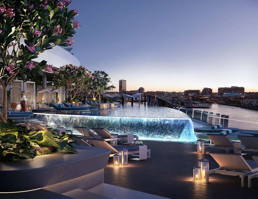 A sun-drenched infinity pool at Crown Towers Sydney on Level 5, featuring white floating daybeds and private cabanas, with the Sydney Harbour Bridge visible in the background.