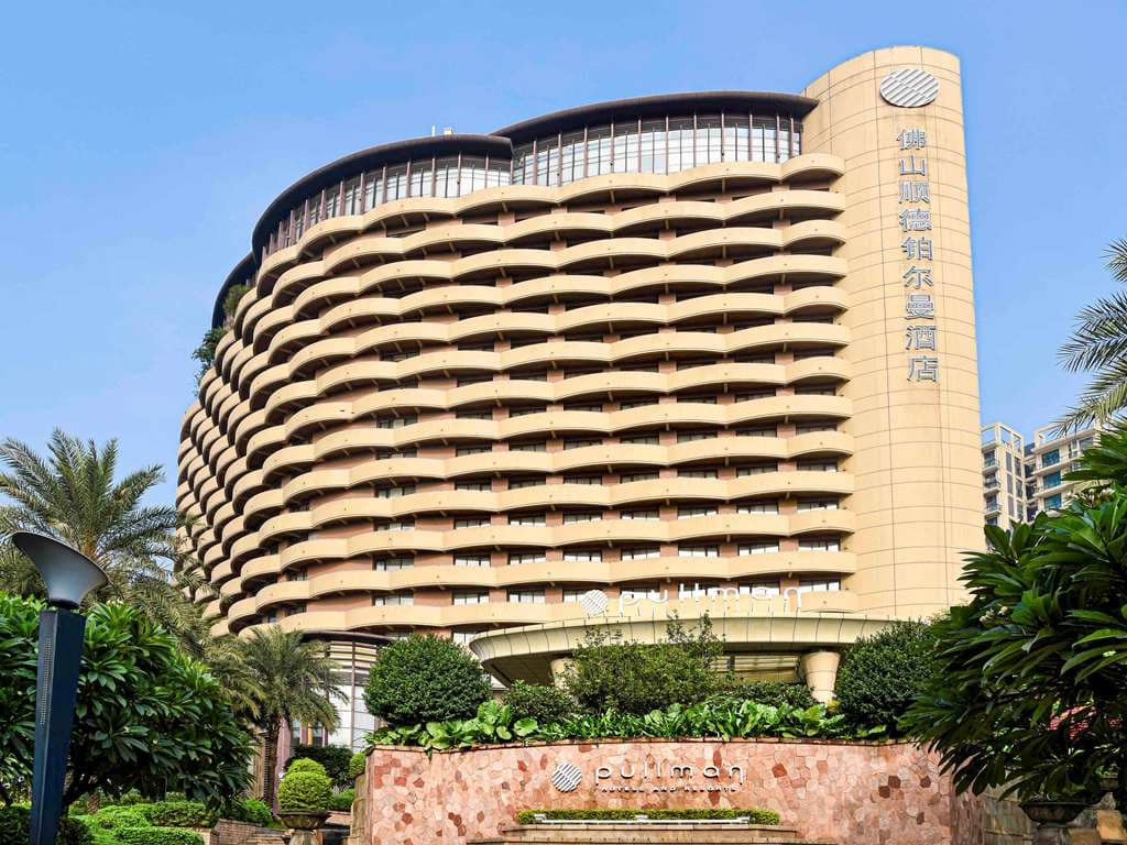 A spacious guest room at Pullman Foshan Shunde featuring a private balcony with city views and soft, warm lighting.
