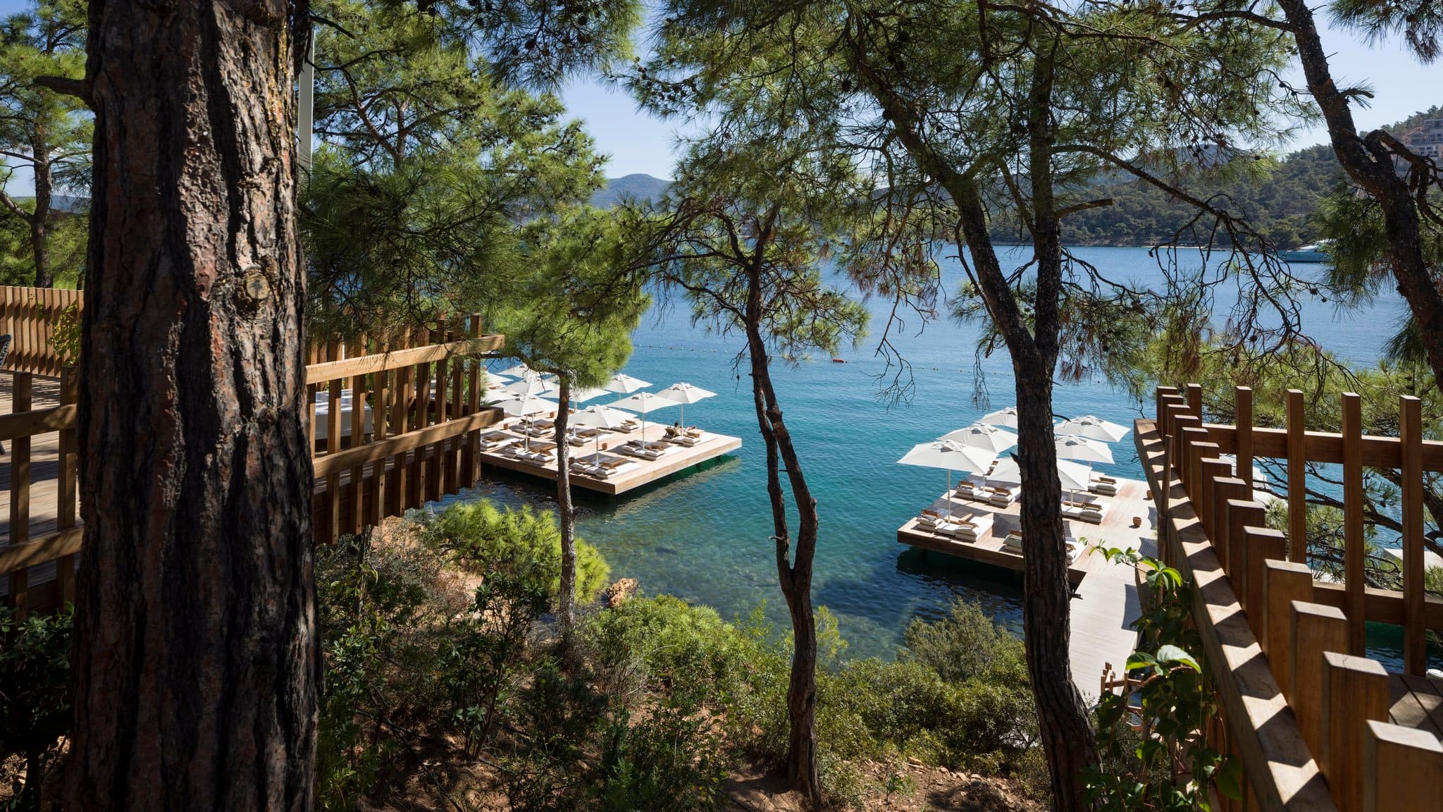 Bodrum Loft's tiered stone villas cascading down a pine-covered hill toward the Aegean Sea, featuring the floating wooden sun decks.