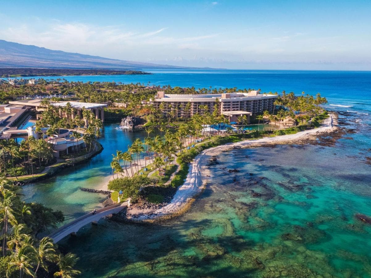 Mahogany canal boat gliding through the Hilton Waikoloa Village waterways at sunset near Buddha Point.