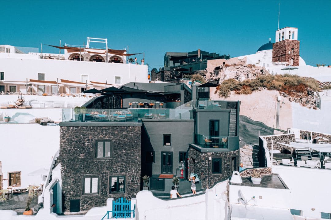 The jet-black architecture of Kivotos Santorini contrasting against the blue Aegean sea, with the infinity pool glowing red at twilight.