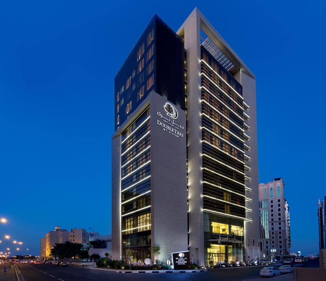 A sleek, modern hotel room with floor-to-ceiling corner windows overlooking the Doha skyline and the National Museum of Qatar structure.