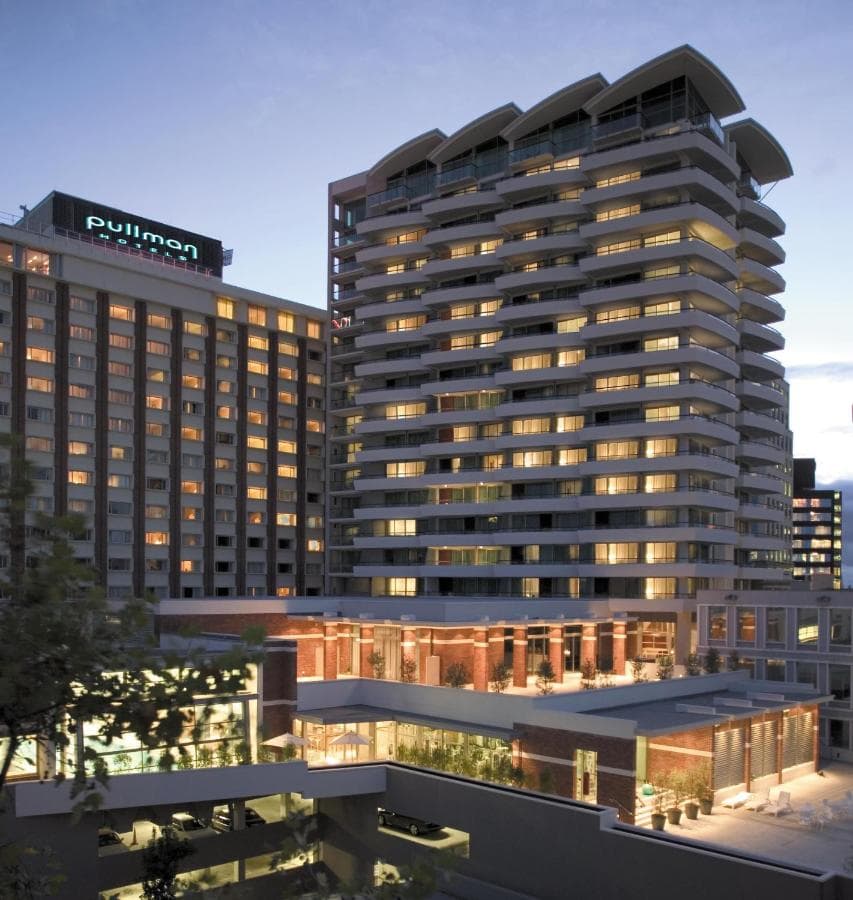 The 25-meter indoor lap pool at Pullman Auckland, featuring a retractable glass wall and lounge chairs on the sun terrace.