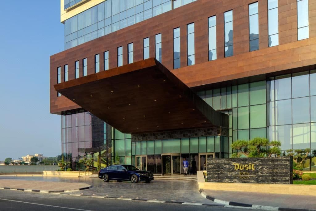 Sunlight flooding a spacious Dusit Doha Hotel room through floor-to-ceiling windows, highlighting the West Bay skyline.