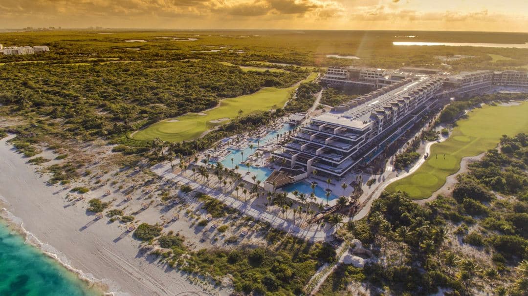 A sleek, modern infinity pool at Atelier Playa Mujeres bordering a mangrove, with guests lounging on in-water beds under a bright Mexican sky.