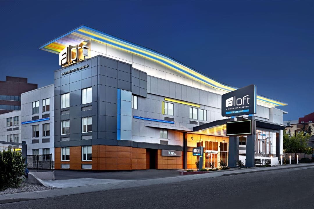 Neon-lit W XYZ Bar at Aloft Calgary University with industrial ceiling pipes and modern lounge seating.