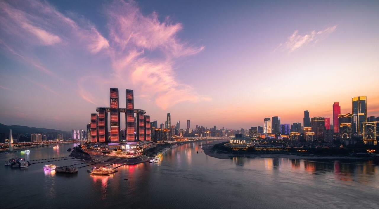 The futuristic Crystal skybridge of Raffles City Chongqing glowing blue at twilight above the river confluence.