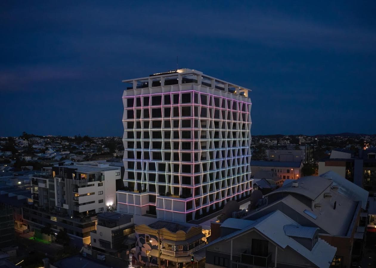 The geometric white façade of Hotel X Brisbane illuminated by purple LED lights at twilight, with the Story Bridge in the background.