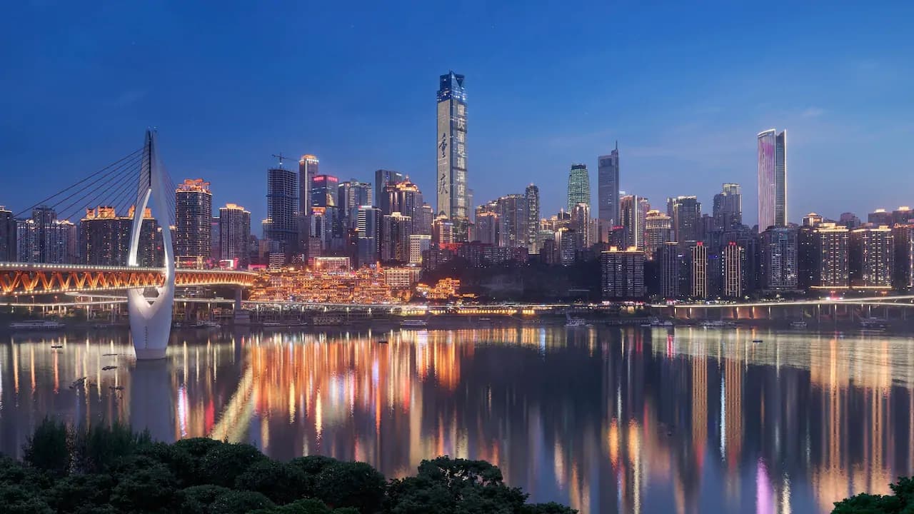 A dramatic silhouette of a guest in a bathtub overlooking the neon-lit Chongqing skyline and river confluence from a high floor.