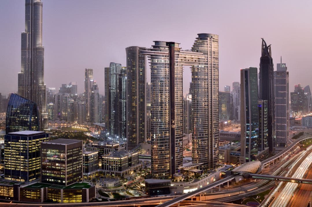 A woman in a red dress on the CÉ LA VI swing with the Burj Khalifa towering in the background at sunset.