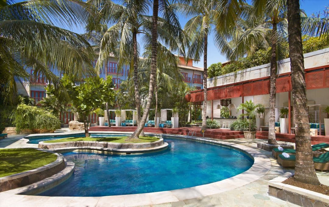 Aerial view of Hard Rock Hotel Bali's massive free-form swimming pool featuring the central Sand Island and surrounding cabanas.