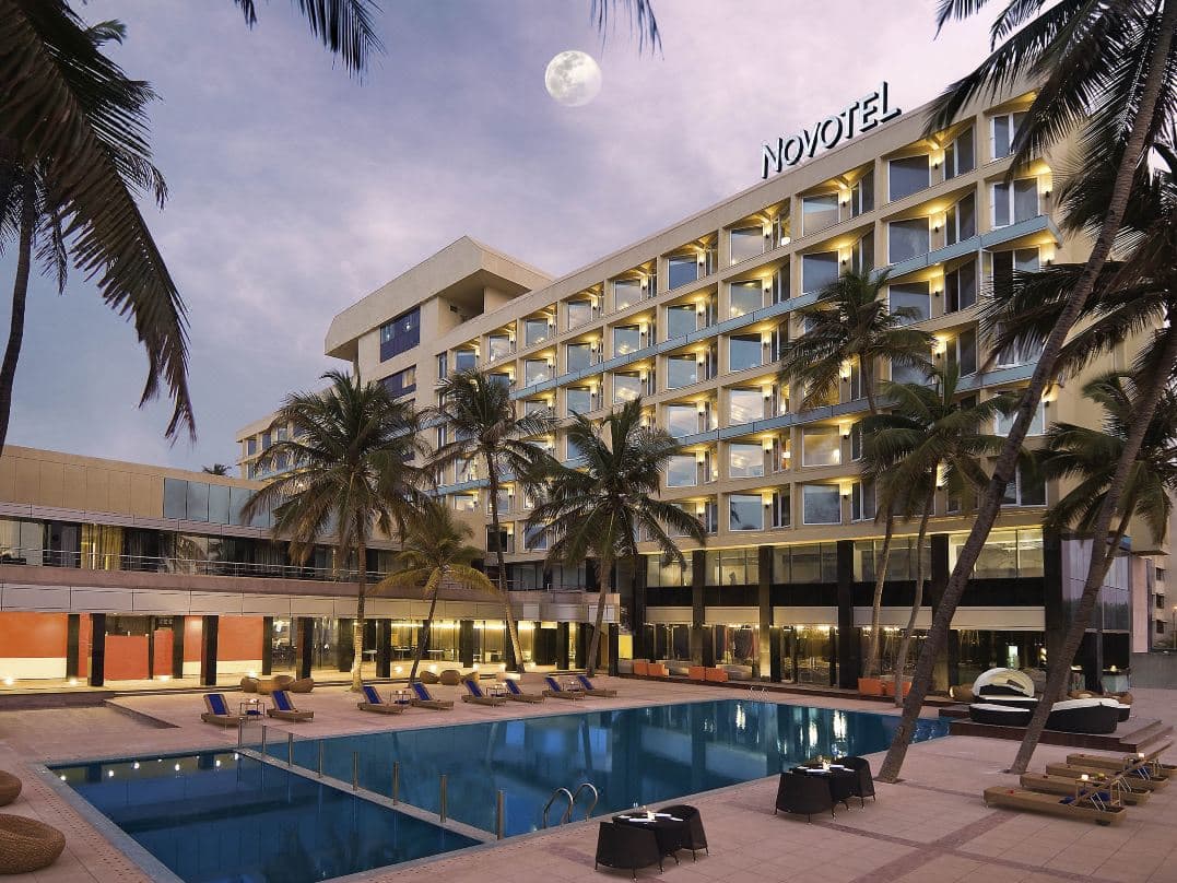 Golden hour view from the Novotel Juhu pool deck overlooking the Arabian Sea, with silhouette of palm trees and Gadda Da Vida lounge.