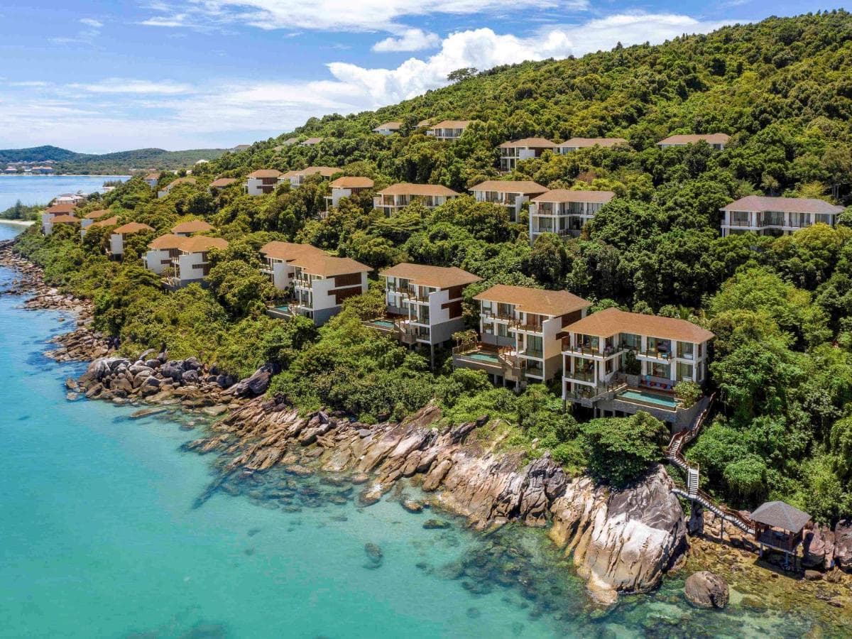 Aerial view of Premier Village Phu Quoc Resort on Ong Doi Cape, featuring white villas with private pools situated between two ocean bays at sunset.