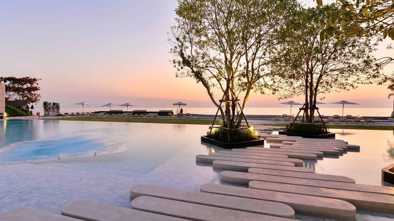 Veranda Resort Pattaya infinity pool with artificial beach elements overlooking the ocean at sunset.