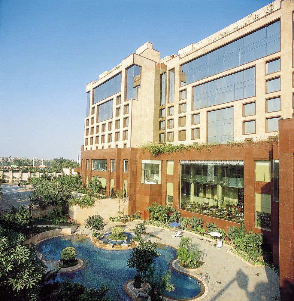 The Sheraton New Delhi's Blue Bay outdoor pool surrounded by lush greenery and stone waterfall landscaping.