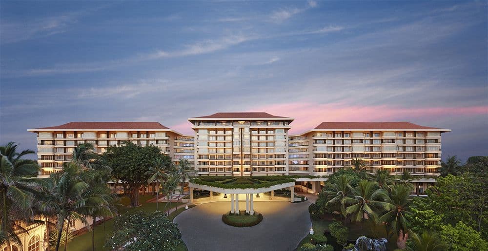 View of Taj Samudra's white colonial facade and pool deck from the Galle Face Green promenade at sunset.