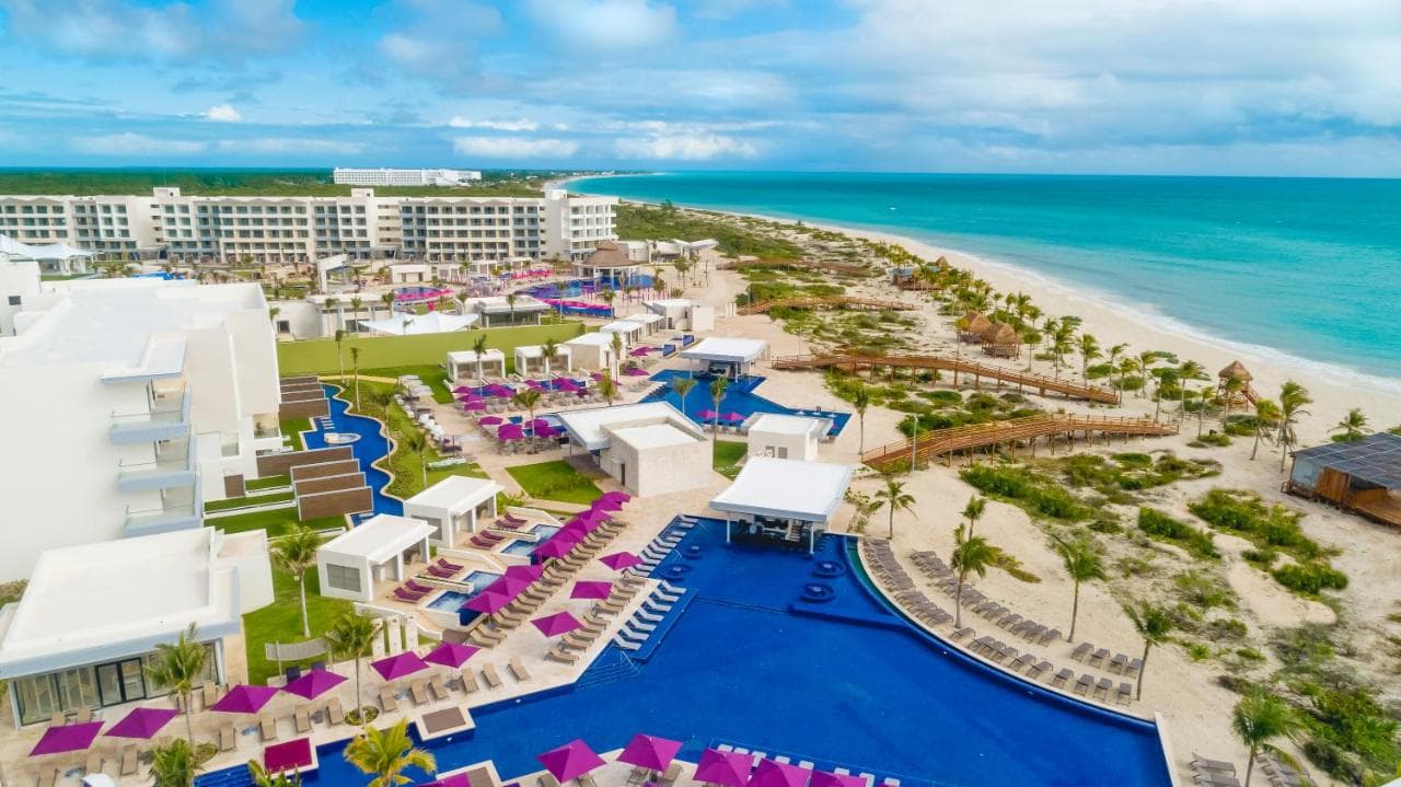 A vibrant view of the Jurassic Splash Park at Planet Hollywood Cancun featuring a giant T-Rex prop and water slides under a sunny sky.