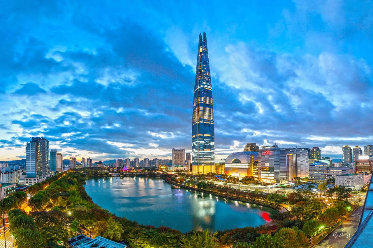 A panoramic view of the Han River from a Signiel Seoul premier room, featuring floor-to-ceiling windows and a plush king bed with Frette linens.