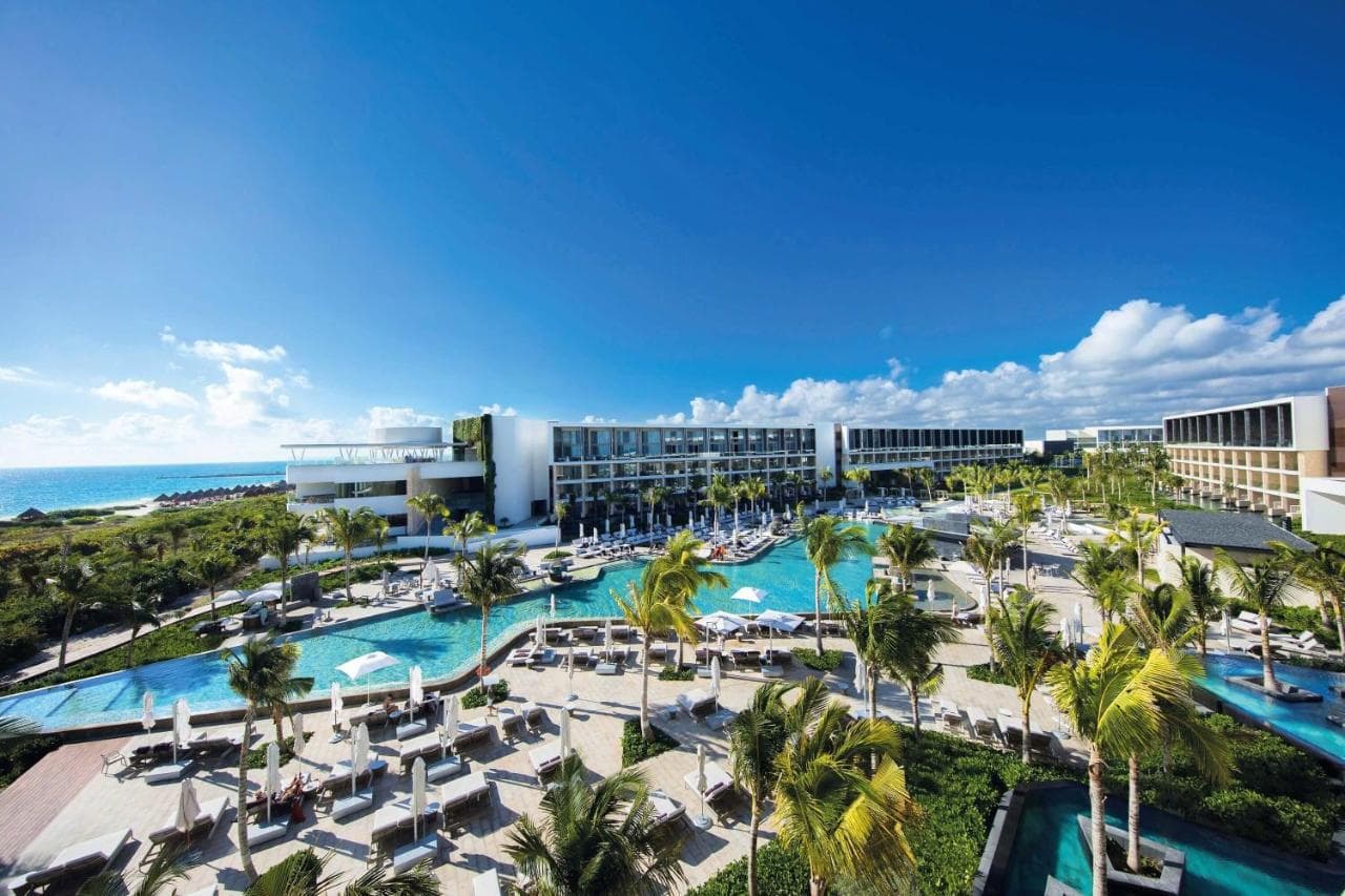 A couple relaxing in a swim-up suite canal pool at TRS Coral Hotel, with modern white architecture and palm trees in the background.