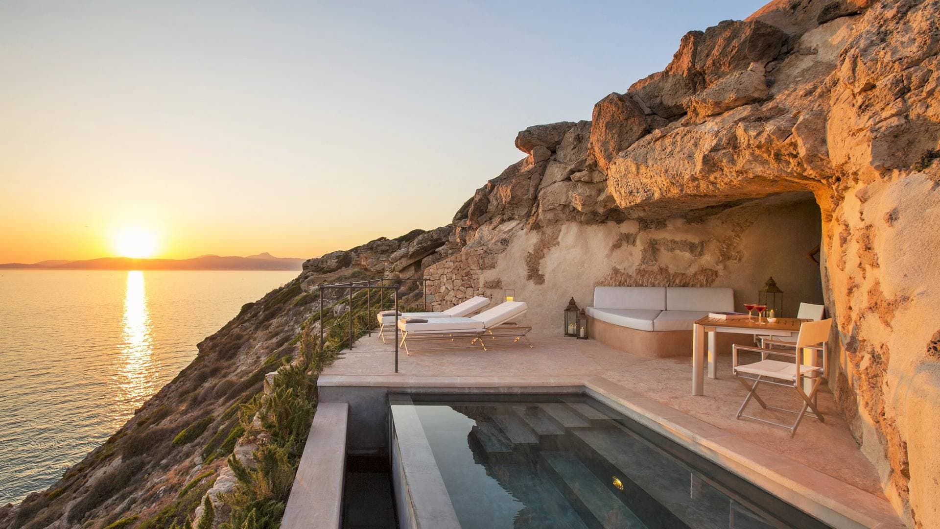 A dramatic view of Cap Rocat's infinity pool carved into sandstone cliffs, overlooking the deep blue Bay of Palma at sunset.