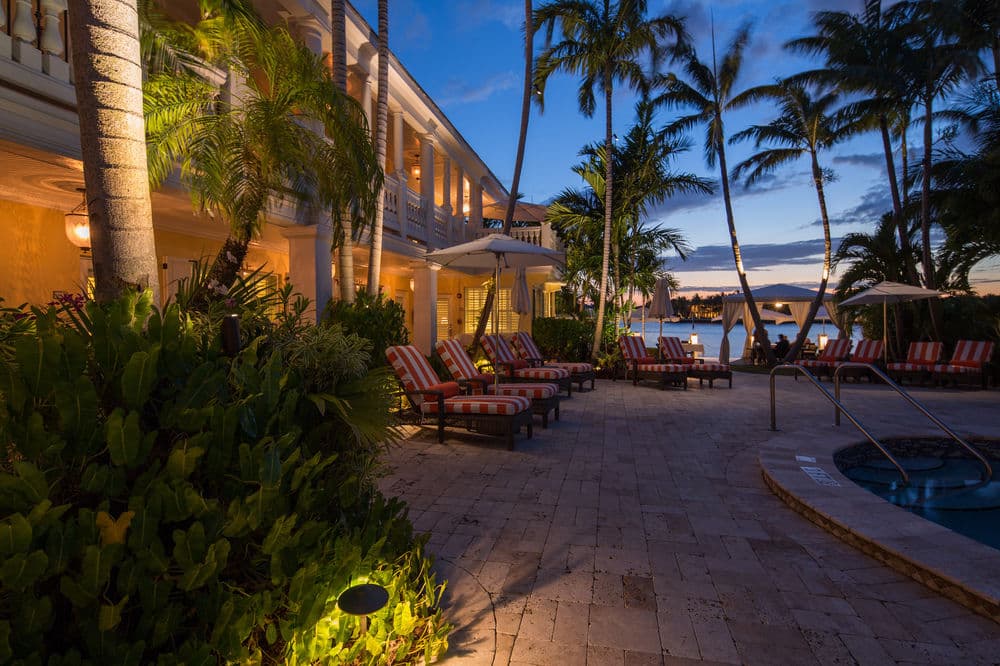 A serene, kidney-shaped pool at The Pillars Hotel bordered by lush tropical greenery and the Intracoastal Waterway at twilight.