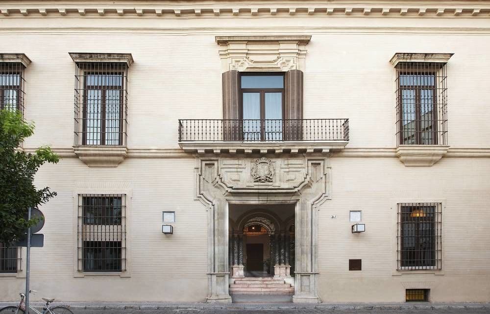 A sun-drenched private rooftop terrace at CoolRooms Palacio de Villapanés featuring white lounge seating and a direct view of the Giralda tower.