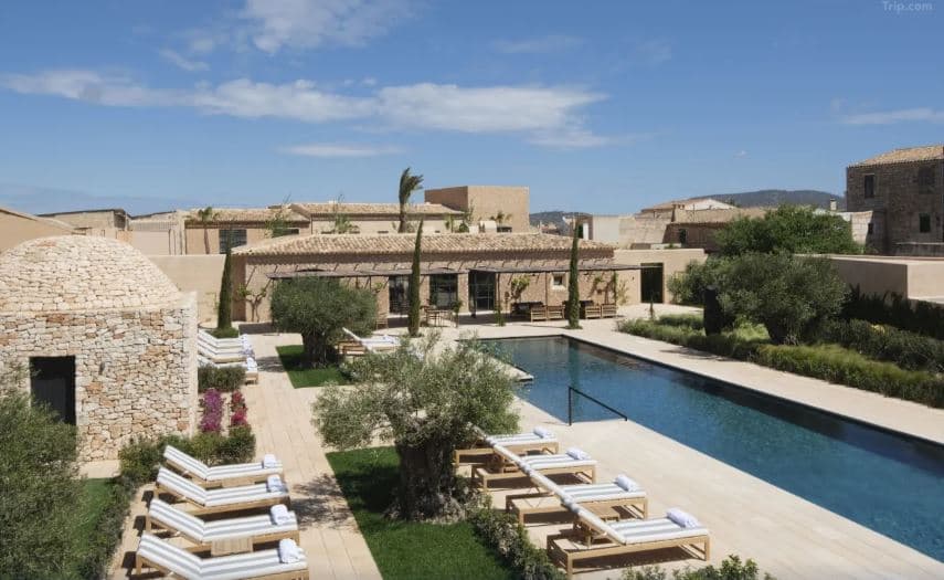 A serene 25-meter outdoor pool at Can Ferrereta lined with cypress trees and stone walls under the Mallorcan sun.