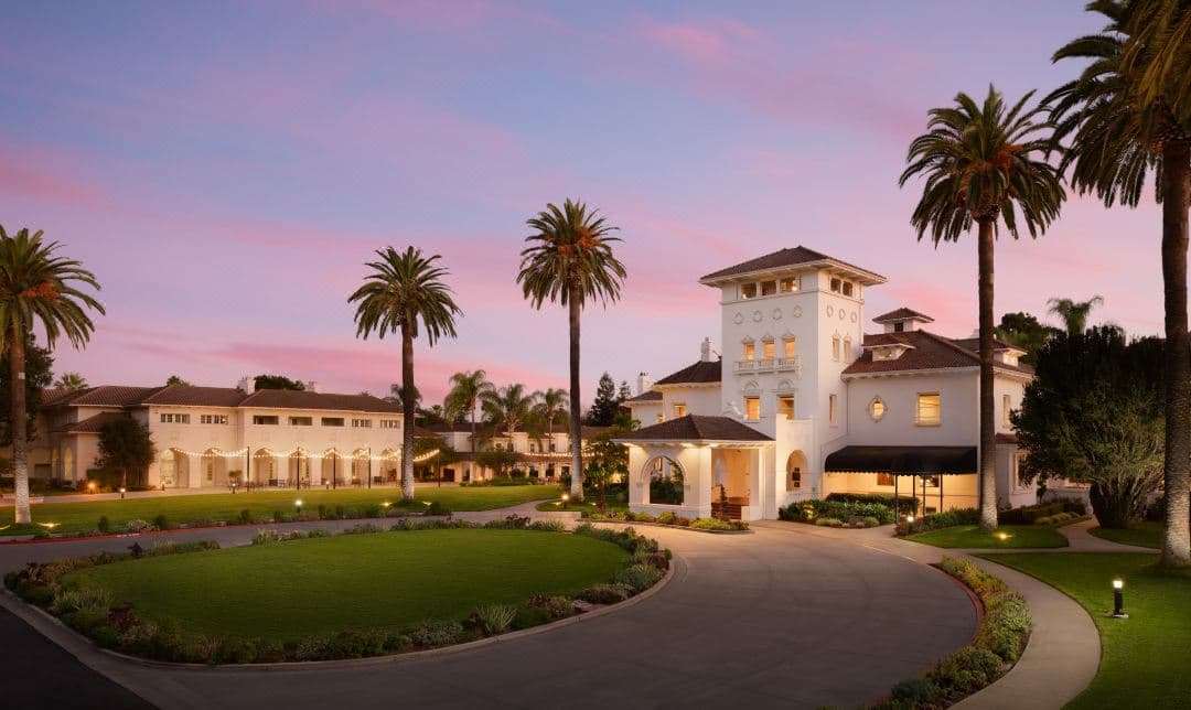The historic Spanish Colonial facade of Hayes Mansion at dusk, framed by palm trees and the illuminated outdoor pool.