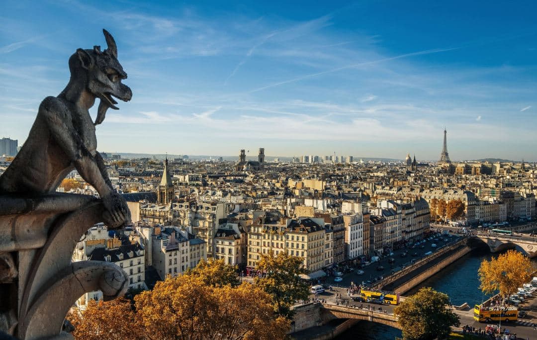 A woman in a white robe standing on a wrought-iron balcony at Hotel Villa Marquis, looking out at the Eiffel Tower during sunrise.