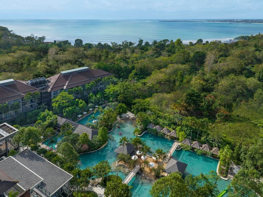 Aerial view of the massive lagoon pool at Mövenpick Jimbaran with swim-up hammocks and lush tropical landscaping.