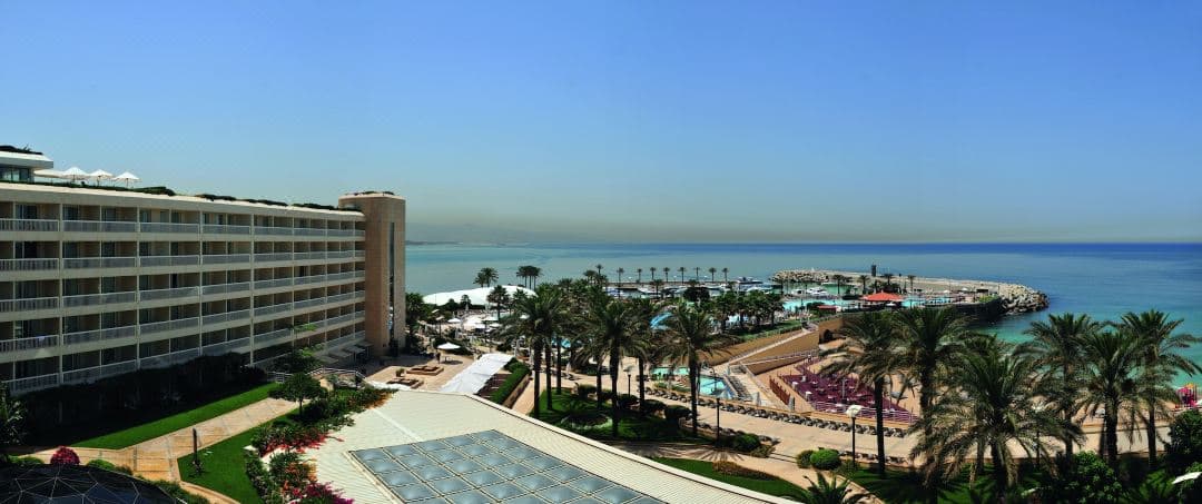 Aerial view of the Olympic-sized swimming pool at Mövenpick Hotel Beirut meeting the Mediterranean Sea at sunset.