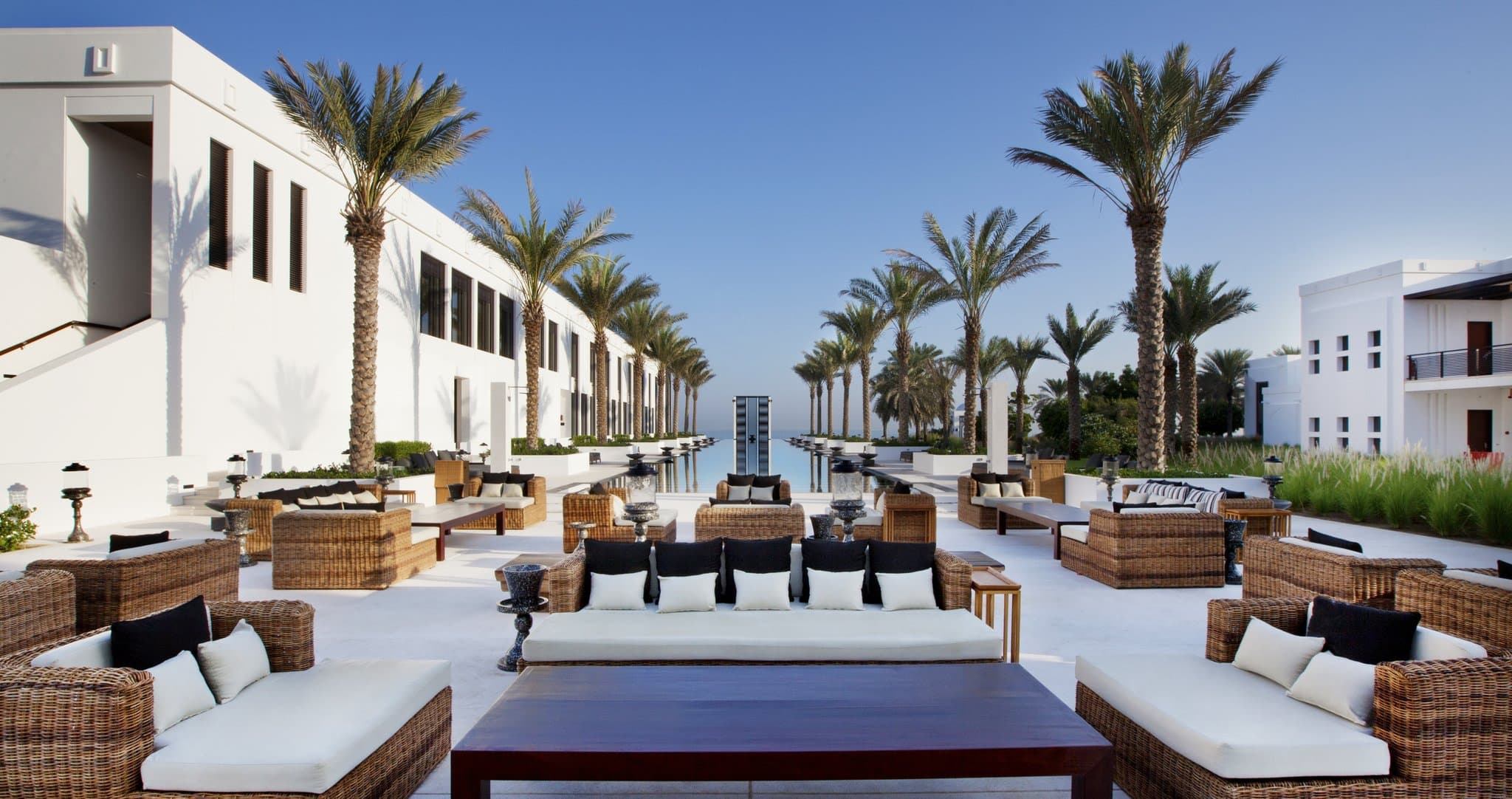 Symmetrical view of The Chedi Muscat's 103-meter Long Pool flanked by palm trees and white cabanas under a dusk sky.
